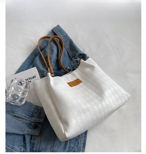 Detail view of white quilted tote bag with brown leather handles and fashion logo