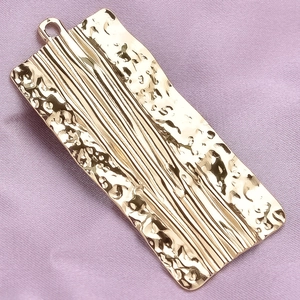 Detail shot of rectangular gold pendant with hammered texture on purple fabric