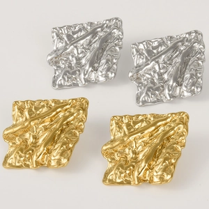 Macro detail of irregular pleated texture on gold and silver square stainless steel earrings