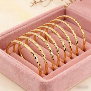 Detailed view of seven gold bangles with diamond-cut patterns in a velvet jewelry box