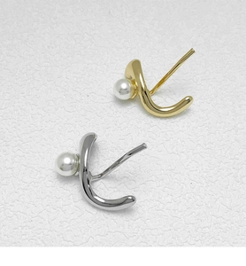 Detailed view of curved gold and silver stud earrings featuring white pearls on white background