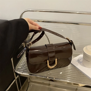 Retro dark brown patent leather shoulder bag with gold horseshoe buckle held by a model