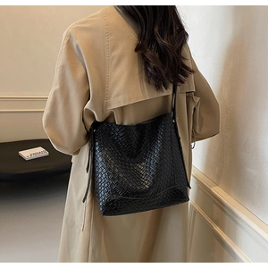 Detail of a large black crocodile pattern tote bag shown over the shoulder of a beige coat