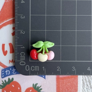 Detailed view of mini resin cherries in red white and pink with green leaves on scale mat
