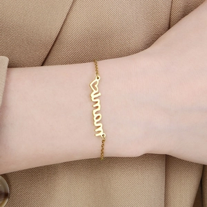 Detail of a gold mama letter bracelet with heart charm worn on a female wrist