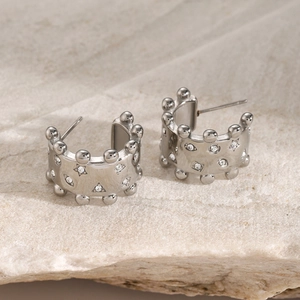 Close-up of silver earrings with geometric zircons and beaded edge on white stone