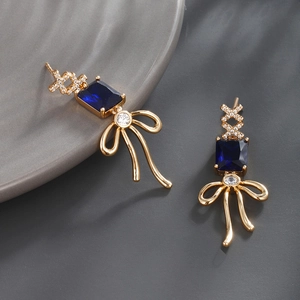 Detail of luxury gold earrings featuring blue square stones and sparkling zircon bows