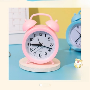 Detail of pink mini alarm clock with dual-bell design on wooden stand