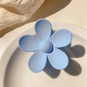 Detailed view of a matte light blue flower-shaped hair claw clip on a white ceramic plate
