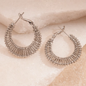 Macro detail of silver geometric hoop earrings with textured finish on white stone