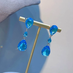Elegant blue teardrop earrings with three-tier moissanite stones on a gold display stand