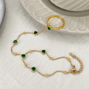Gold finger ring bracelet with green heart gemstones on a white textured background