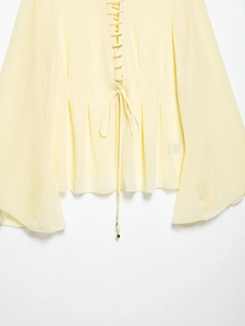 Close-up of the delicate lace-up tie and flared cuff details on a pale yellow chiffon blouse
