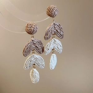 Detailed view of bohemian layered raffia leaf earrings with golden accents on a warm backdrop