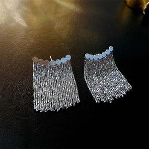 Macro shot of silver geometric fringe stud earrings with long metal chain tassels on dark background