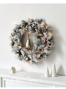 Close-up of frosted Christmas wreath with LED lights, pine cones, and a metal bell