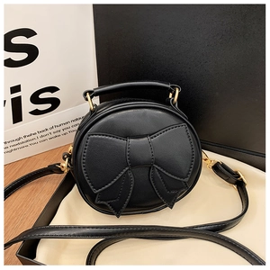 Detail of a mini round kids crossbody bag in black leather with a large bow and gold hardware
