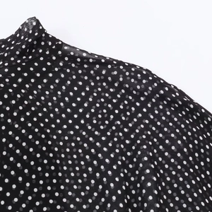 Dettaglio del tessuto in chiffon nero trasparente con pois bianchi su scollo e spalla