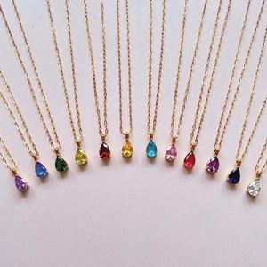 Golden titanium steel necklaces with colorful teardrop birthstone pendants on pink background