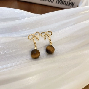 Detail of gold bow earrings with brown tiger eye beads on white pleated fabric