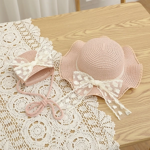 Detail of pink straw hat and matching bag set with large lace bows and wavy brim edges