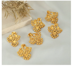 Macro shot of gold fan-shaped pine leaf stud earrings on a textured fabric background