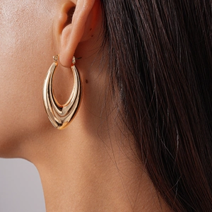 Close-up of a large gold polished hollow teardrop earring worn by a model