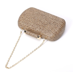 Close-up of woven texture and golden metal chain strap on beige straw evening clutch