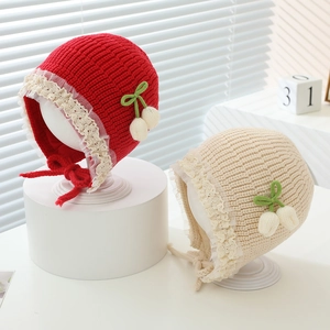Detailed close-up of knit baby hat with floral lace trim and cozy earflaps in red and beige