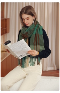 Close-up of green and brown plaid scarf with fringe detail worn in a cozy indoor setting