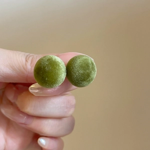 Detailed close-up of green flocked spherical stud earrings with velvet texture