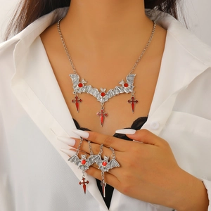Close-up of gothic silver bat necklace and red cross ring set worn on neck and finger