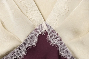 Detailed close-up of cream and burgundy satin fabric with delicate white eyelash lace trim