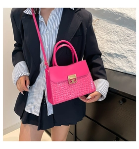 Pink crocodile-embossed handbag featuring a gold square lock and adjustable shoulder strap