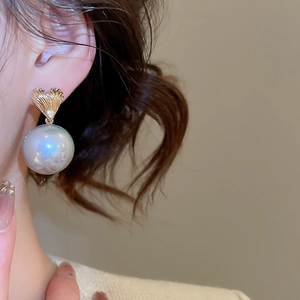 Detailed view of elegant gold heart earring with iridescent pearl on model's ear