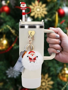 Cream Stanley cup with Christmas Santa charm and plush ball accessory in hand