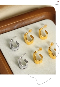 Detailed close-up of wavy irregular gold and silver earrings on a beige velvet tray