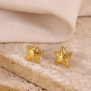 Macro detail of gold starfish stud earrings with embossed texture on stone and fabric