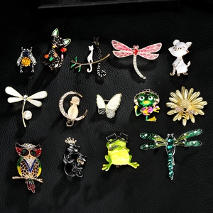 Flat lay of diverse animal and flower enamel brooches on black textured leather surface