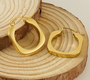 Detailed macro view of gold plated geometric U-shaped chunky hoop earrings on wood base