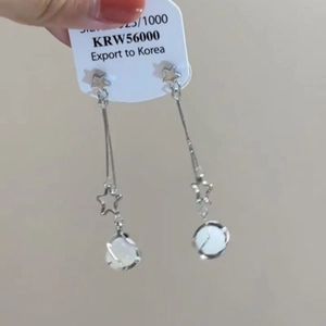 Detail of silver tassel drop earrings featuring star studs and white cat eye beads