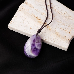 Natural teardrop amethyst pendant necklace on stone background with brown woven cord