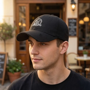 Men's black baseball cap with distressed brim and embroidered logo in outdoor cafe setting