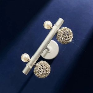 Detail of elegant earrings with white pearl and rhinestone ball on a blue velvet stand