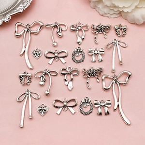 Silver bow and heart metal charms collection for DIY jewelry on a pink background