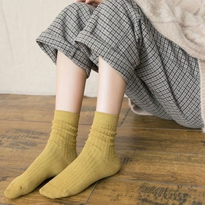 Close-up of mustard yellow cotton knit mid-calf socks with ribbed cuffs on wooden floor