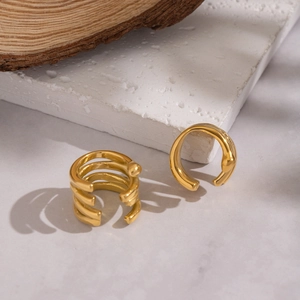 Golden multi-layer spiral ear cuff with geometric lines on a textured stone surface