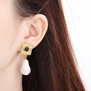 Close-up of golden square hammered earring with black stone and baroque pearl on model