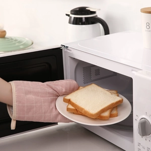 Pink checkered heat resistant oven glove taking fresh toast out of a white microwave
