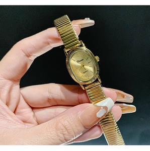 Detail of elegant gold oval quartz watch with stretch metal band worn on a wrist